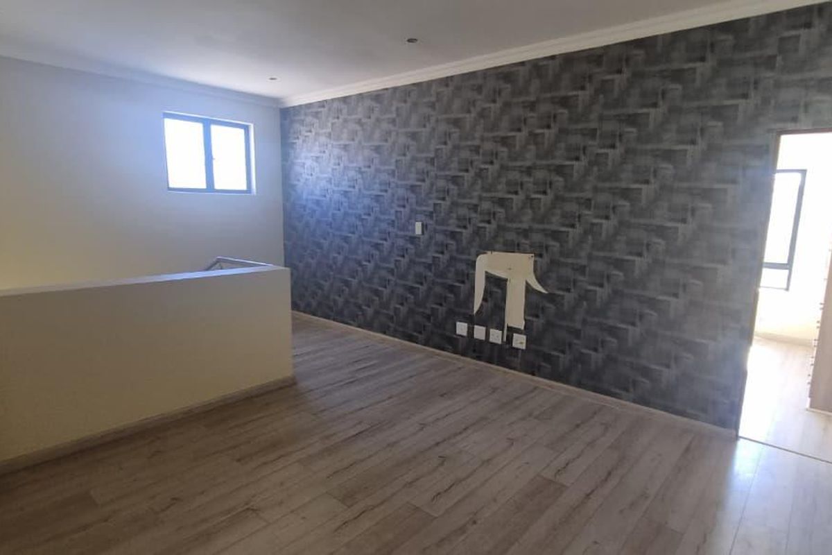 An open-plan living area featuring wood-look laminate flooring, a textured feature wall, and a staircase landing with a low partition wall.