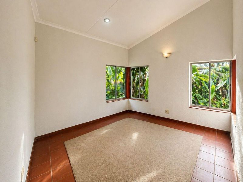 A bright, empty bedroom featuring vaulted ceilings, tiled flooring, and large windows providing natural light and garden views.