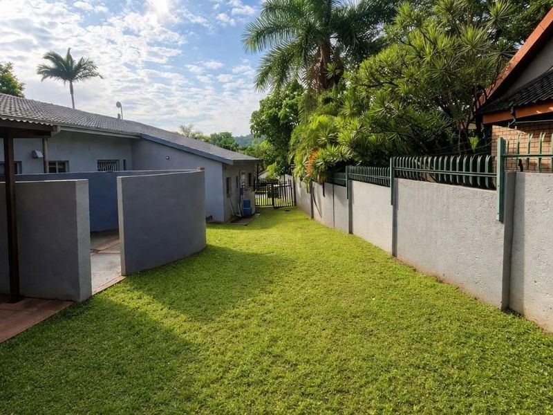 A well-maintained side garden area featuring a manicured lawn, perimeter boundary walls with metal fencing, and a paved patio section.