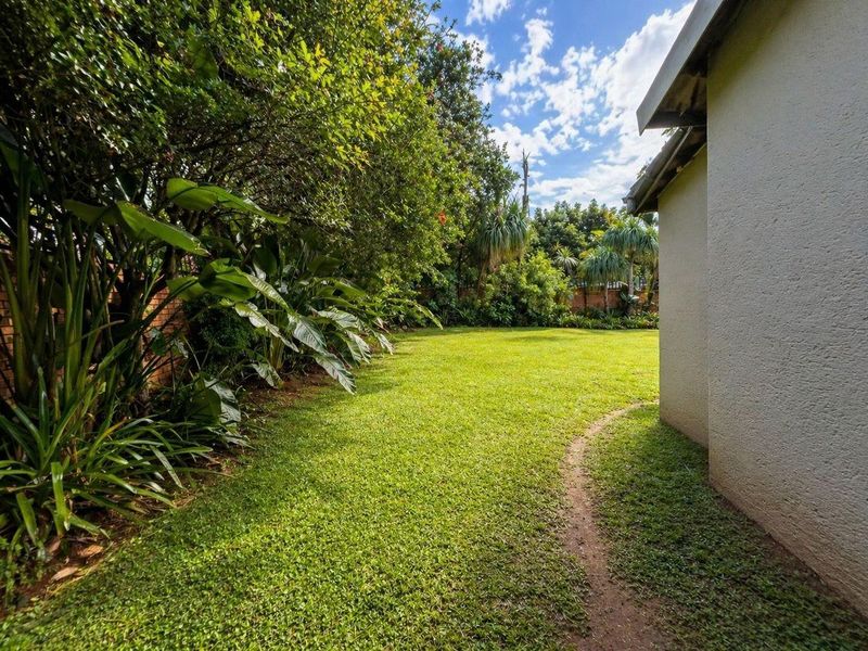 A well-maintained private garden area featuring lush greenery, mature trees, and a manicured lawn adjacent to the side of the house.