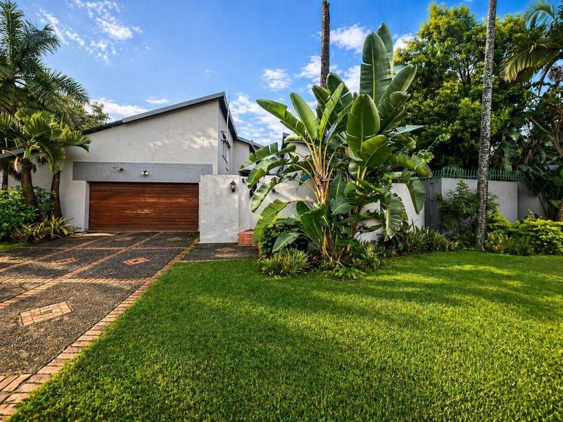 Front exterior view of the property featuring a paved driveway, wooden garage door, and established garden landscaping.