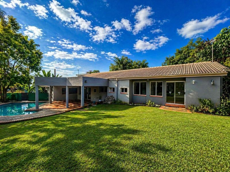 Rear view of the property featuring a spacious lawn, a covered patio area, and an integrated swimming pool.