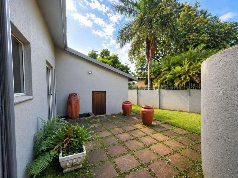 A private rear patio area featuring paved flooring, a small access door, and a landscaped garden border enclosed by a perimeter wall.