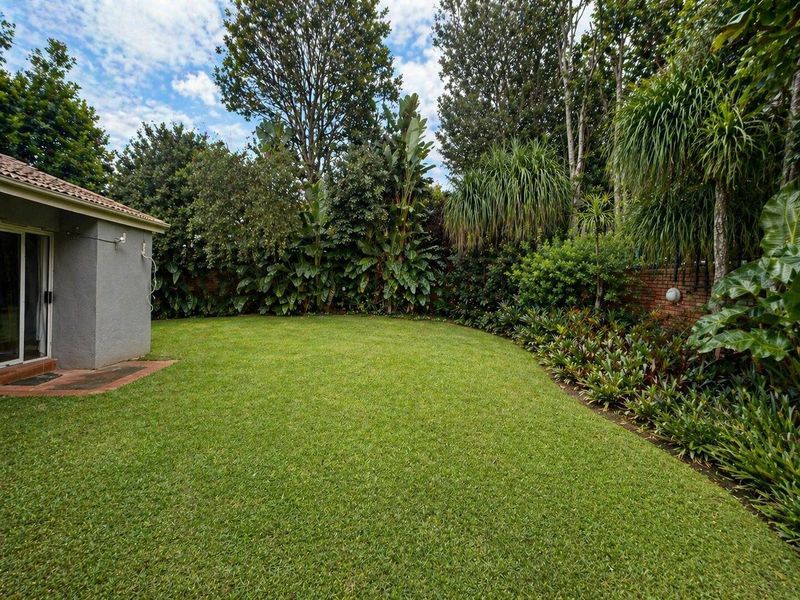 A well-maintained rear garden featuring a lush green lawn, established perimeter landscaping, and a brick boundary wall, adjacent to the home's exterior.