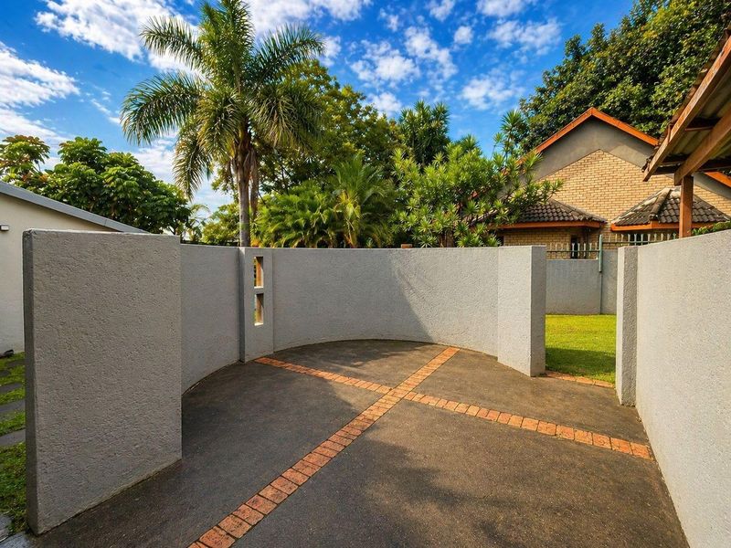A private outdoor courtyard area featuring a curved rendered wall, paved flooring with brick inlay, and access to a landscaped garden.