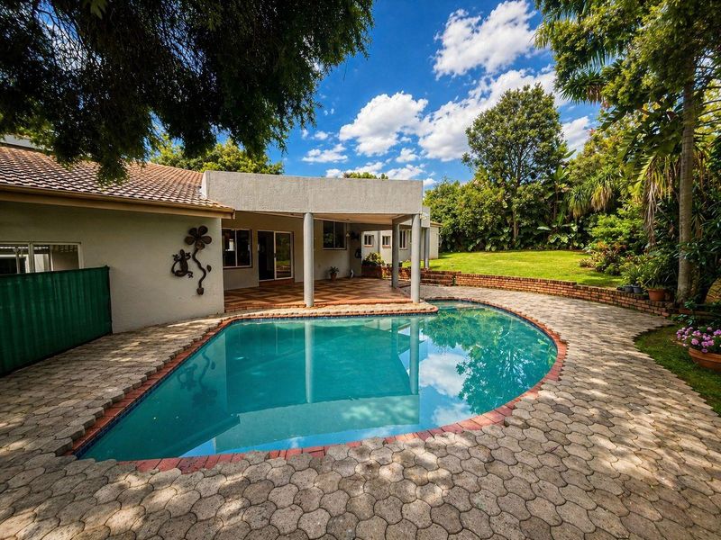 A spacious outdoor entertainment area featuring a covered patio, a swimming pool with paved surround, and a well-maintained garden.