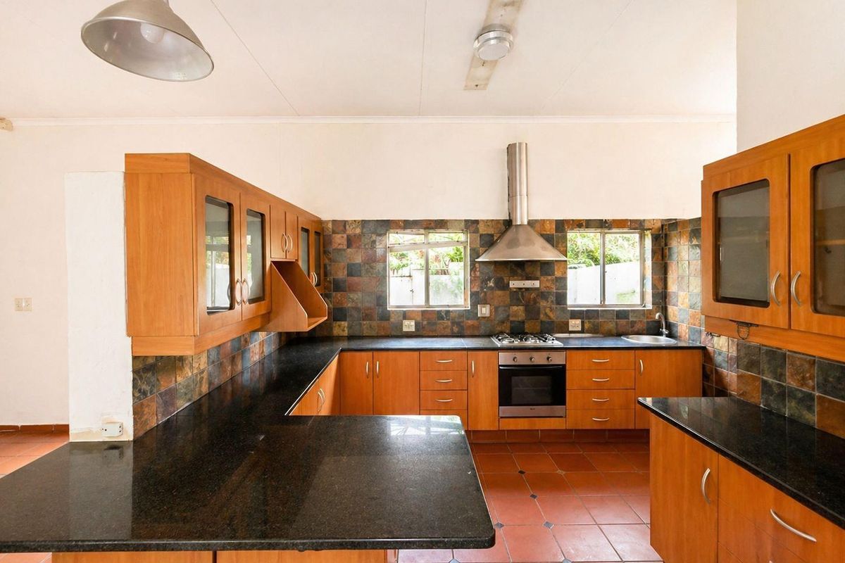 Functional kitchen featuring wooden cabinetry, dark granite countertops, a built-in oven with extractor fan, and decorative slate-style wall tiling.