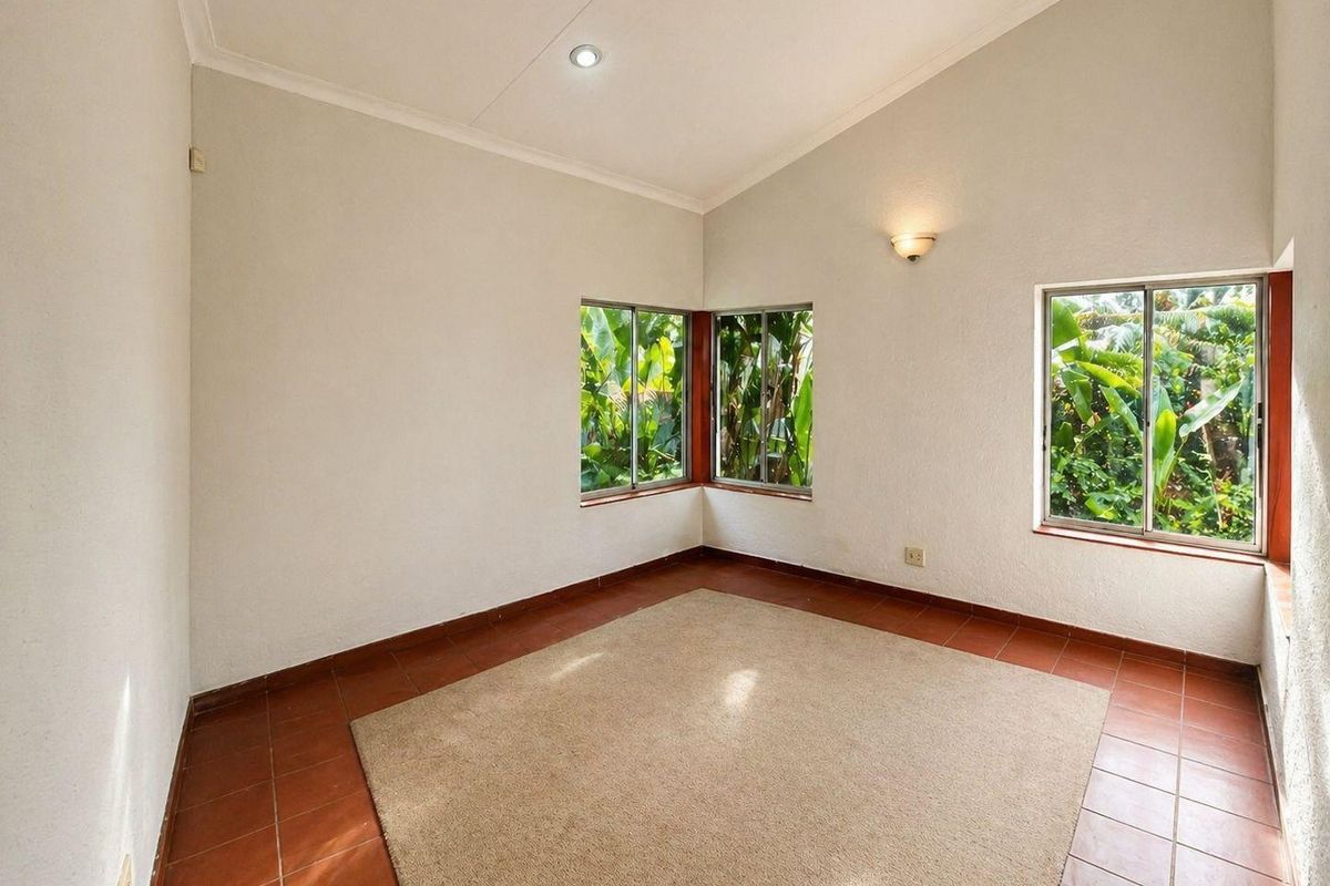 A bright, empty bedroom featuring vaulted ceilings, tiled flooring, and large windows providing natural light and garden views.