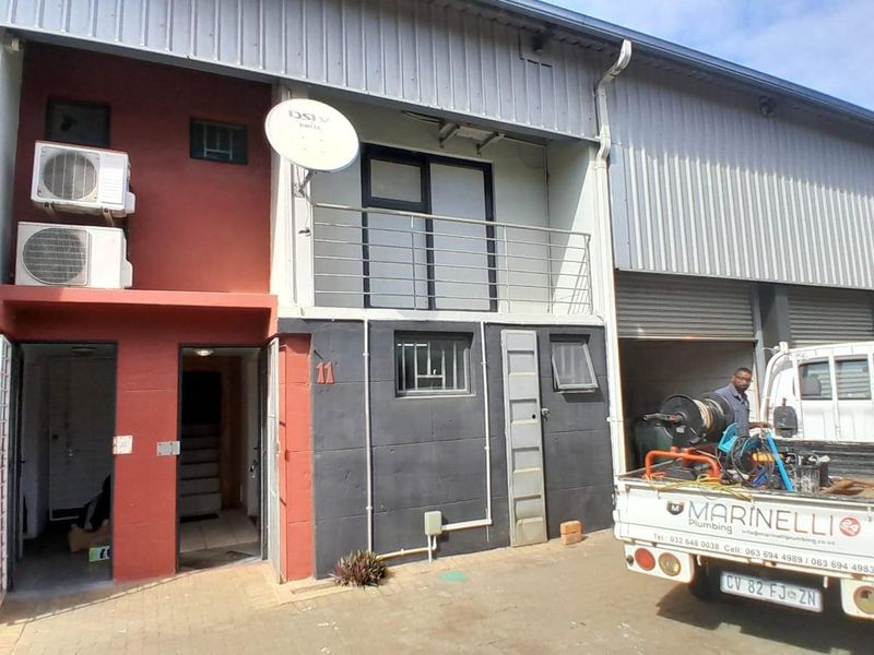 Exterior view of an industrial unit featuring a metal facade, balcony with railing, and ground-level entrance with air conditioning units.