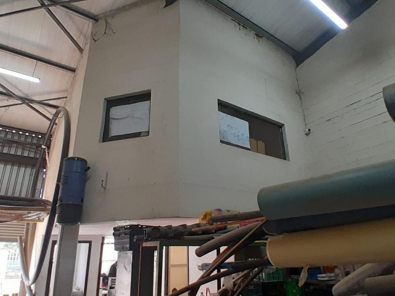 Industrial warehouse interior featuring a mezzanine office structure with exposed steel roof trusses and fluorescent lighting.