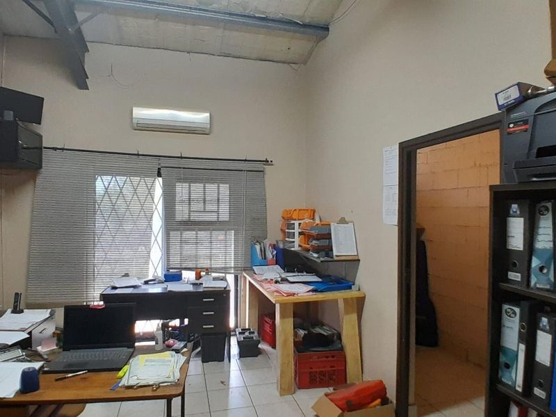 Functional office space featuring tiled flooring, a wall-mounted air conditioning unit, and exposed industrial-style ceiling beams.