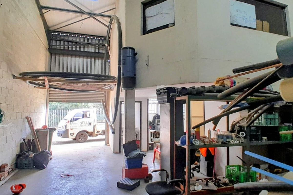 Industrial warehouse space featuring high ceilings, roller shutter door access, and mezzanine level, suitable for storage or workshop operations.