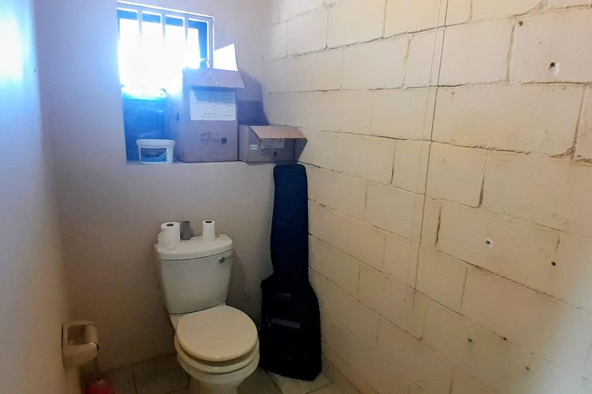 A functional industrial-style restroom featuring a basic toilet, tiled flooring, and exposed concrete block wall construction with a small security-barred window.