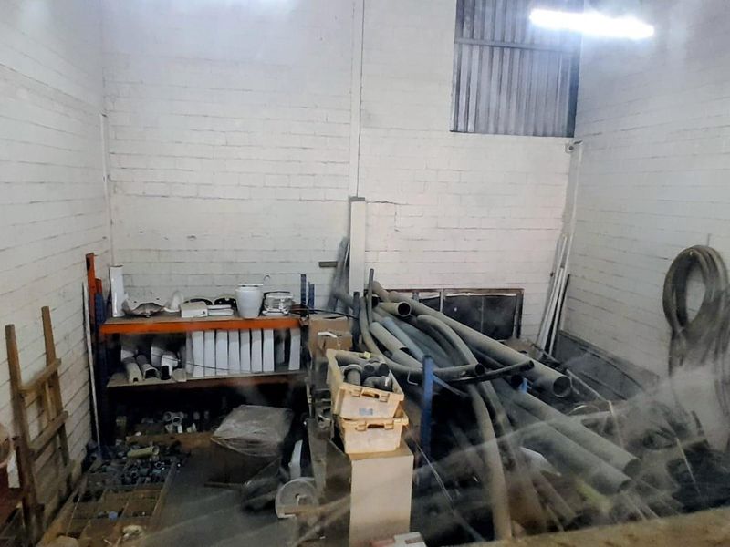 A utility storage space featuring exposed brick walls and industrial shelving, currently used for storing various pipes and construction materials.