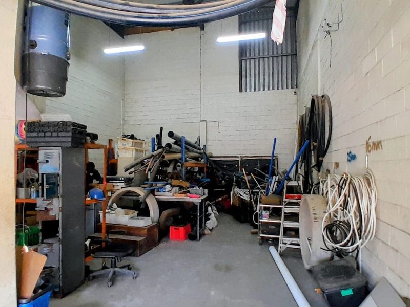 Industrial utility space featuring high ceilings, exposed masonry walls, and fluorescent lighting, suitable for storage or workshop operations.