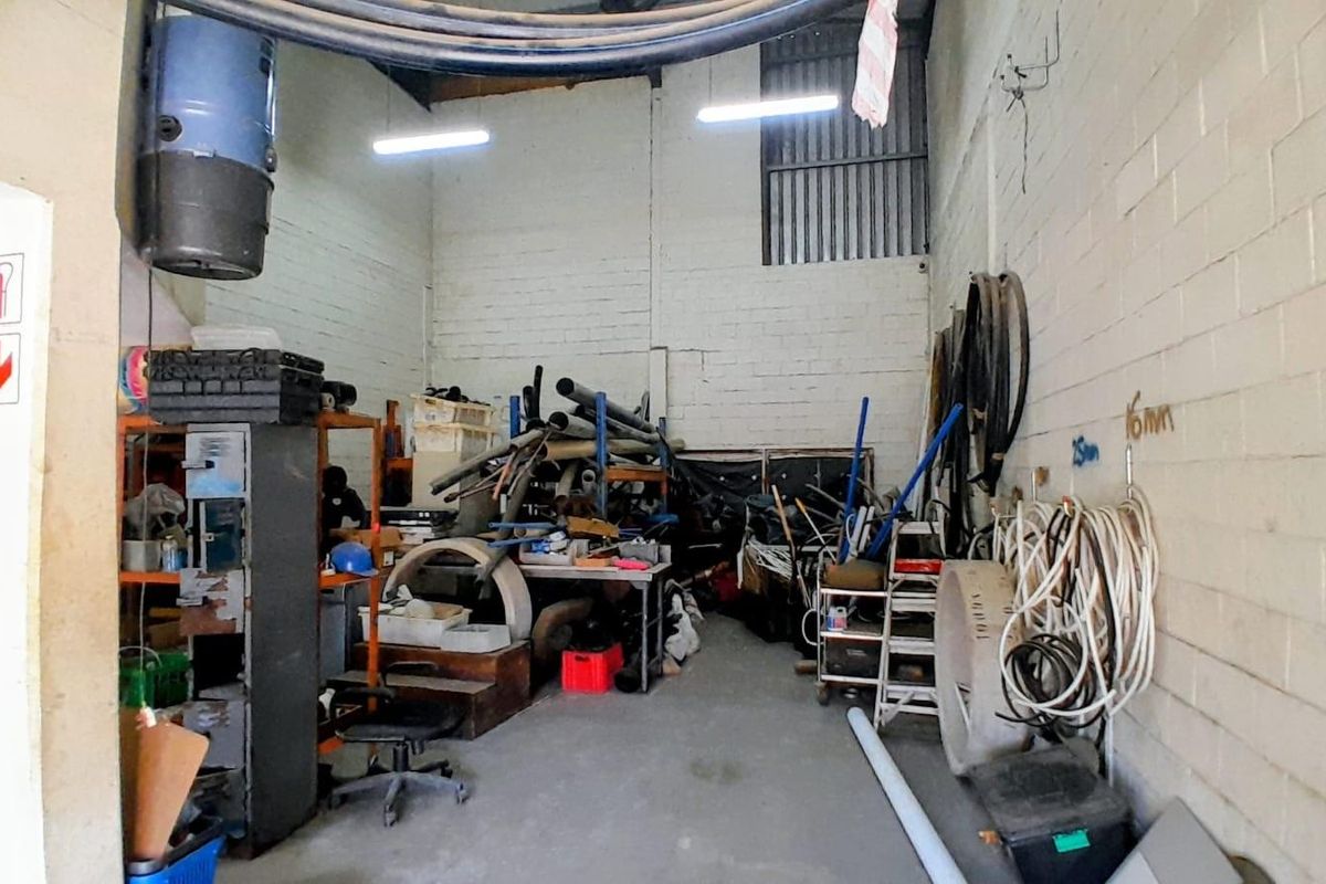 Industrial utility space featuring high ceilings, exposed masonry walls, and fluorescent lighting, suitable for storage or workshop operations.