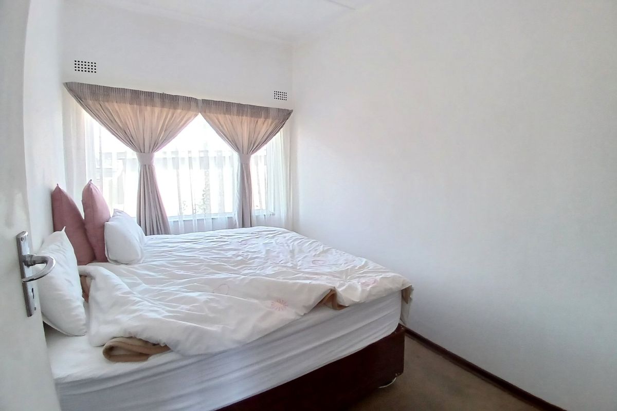 A simple bedroom featuring white walls, a large window with curtains, and ventilation grilles.