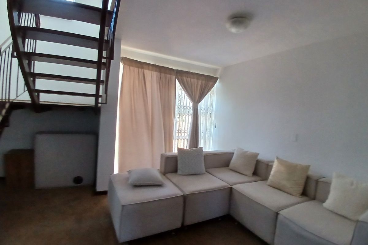 Living room area featuring an open-tread staircase and large window with security gate, providing a bright and functional space.