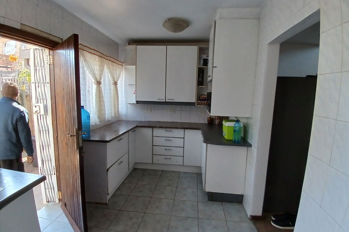 A functional kitchen featuring white built-in cabinetry, laminate countertops, and tiled flooring, offering a practical layout with direct access to the exterior.