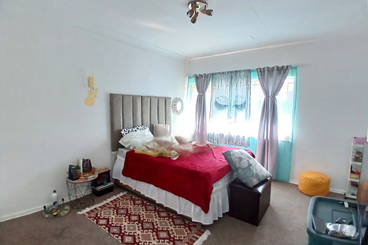 A bedroom featuring a neutral color palette, carpeted flooring, and a window with curtain treatments.