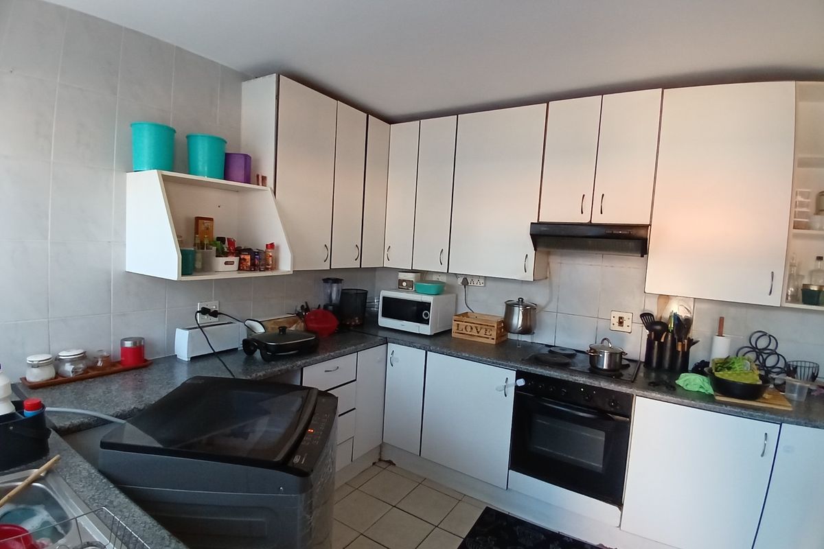 A functional kitchen featuring white cabinetry, a built-in oven, extractor fan, and tiled flooring with ample counter space.