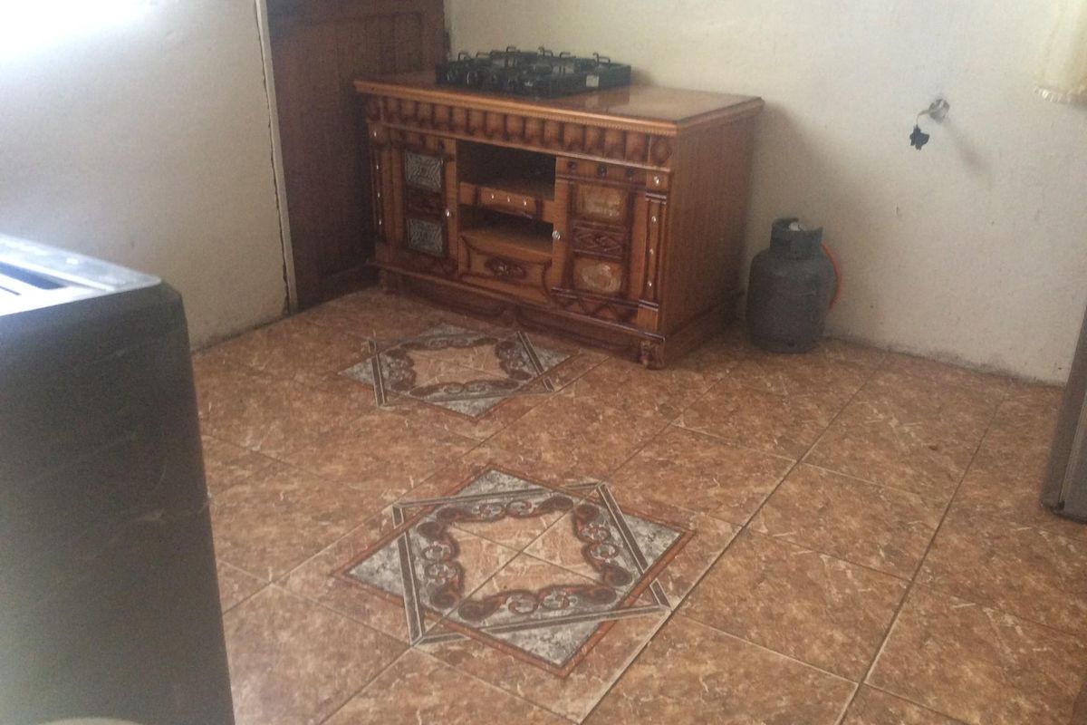A basic kitchen area featuring patterned ceramic floor tiles, a wooden cabinet unit, and exposed electrical points requiring finishing.