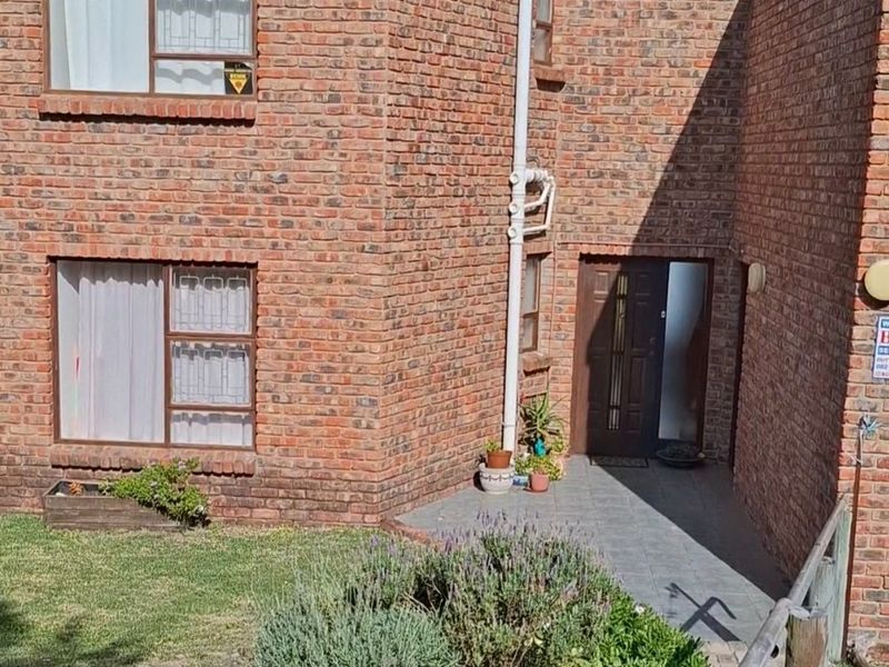 A two-story face-brick residential exterior featuring a paved entrance path, landscaped garden area, and secure front door access.