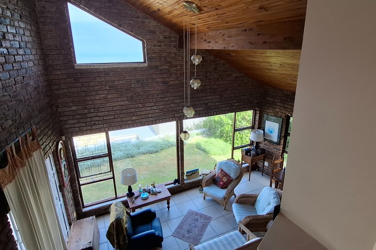 Spacious living area featuring double-volume ceilings with exposed timber beams, large brick feature walls, and expansive windows overlooking the garden.