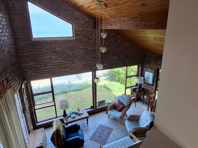 Spacious living area featuring double-volume ceilings with exposed timber beams, large brick feature walls, and expansive windows overlooking the garden.