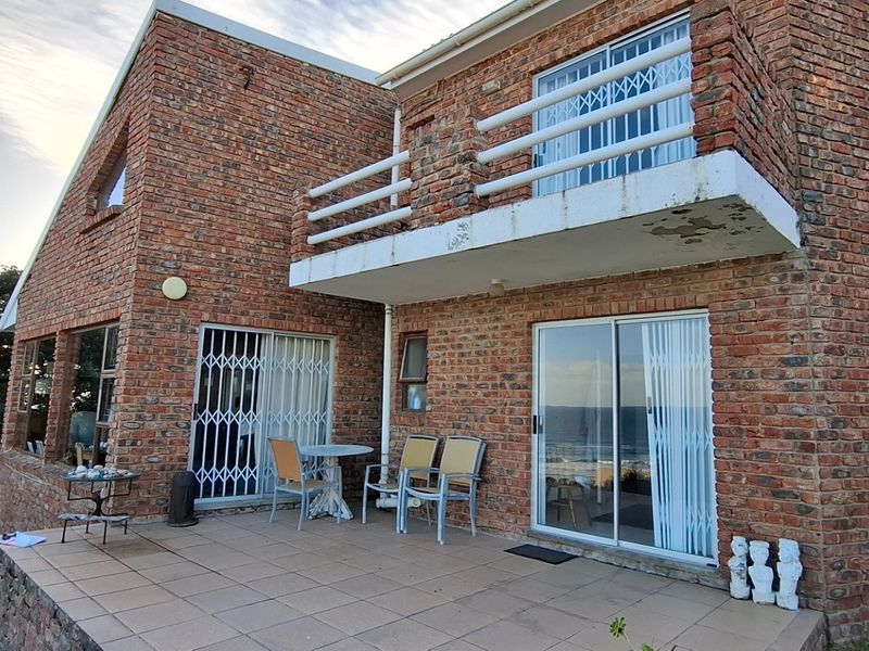 Rear view of a double-story face-brick house featuring a tiled patio and an upper-level balcony with security gates.