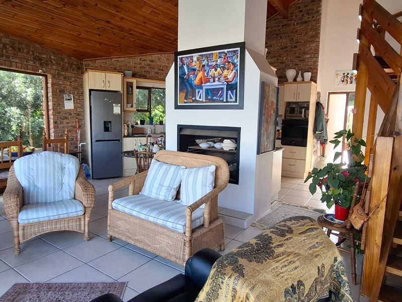 Open-plan living area featuring exposed brick walls, timber-clad vaulted ceilings, a central fireplace, and a wooden staircase leading to the upper level.