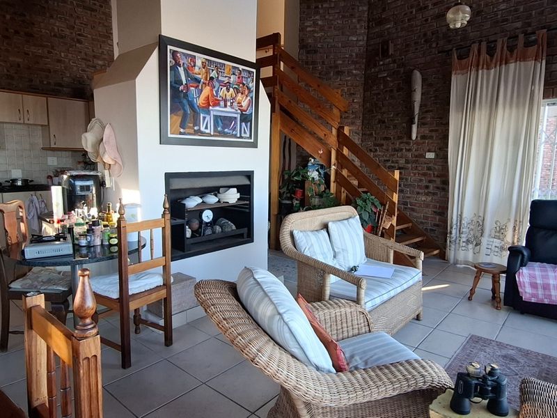 Open-plan living area featuring exposed brick walls, a central fireplace, a functional kitchen with light wood cabinetry, and a staircase leading to the upper level.