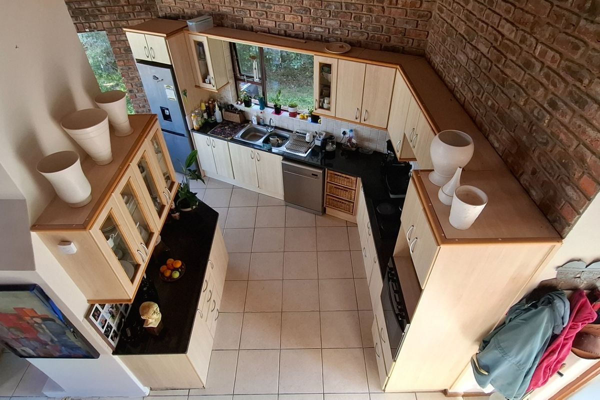 A high-angle view of a kitchen featuring light wood cabinetry, dark granite countertops, tiled flooring, and an exposed brick feature wall.