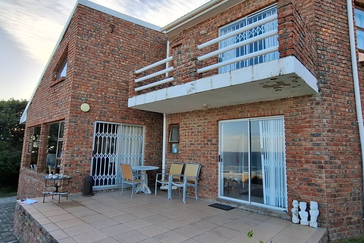 Rear view of a double-story face-brick house featuring a tiled patio and an upper-level balcony with security gates.