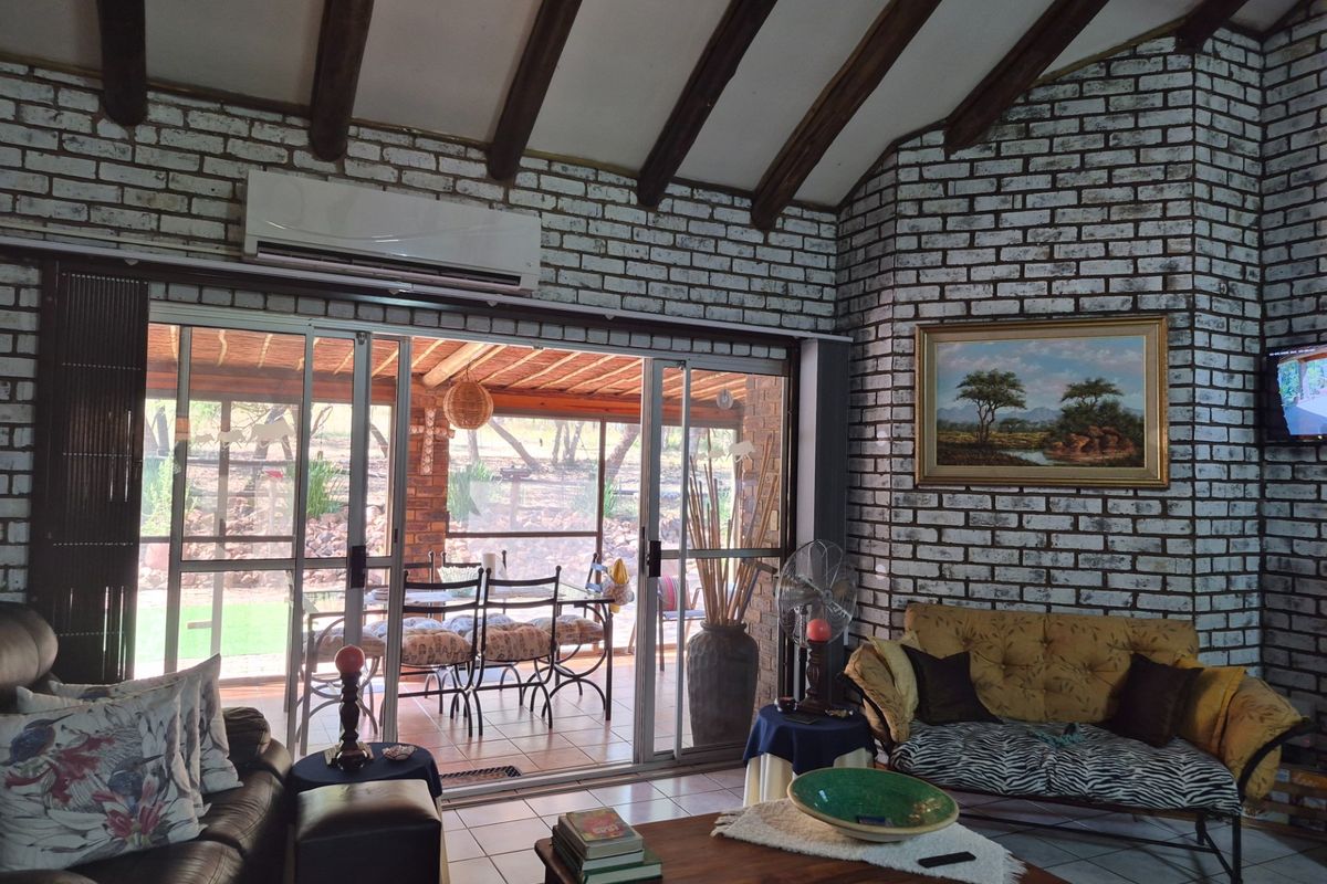 Spacious living area featuring exposed timber ceiling beams, white-washed brick walls, and large sliding glass doors opening onto a covered patio.