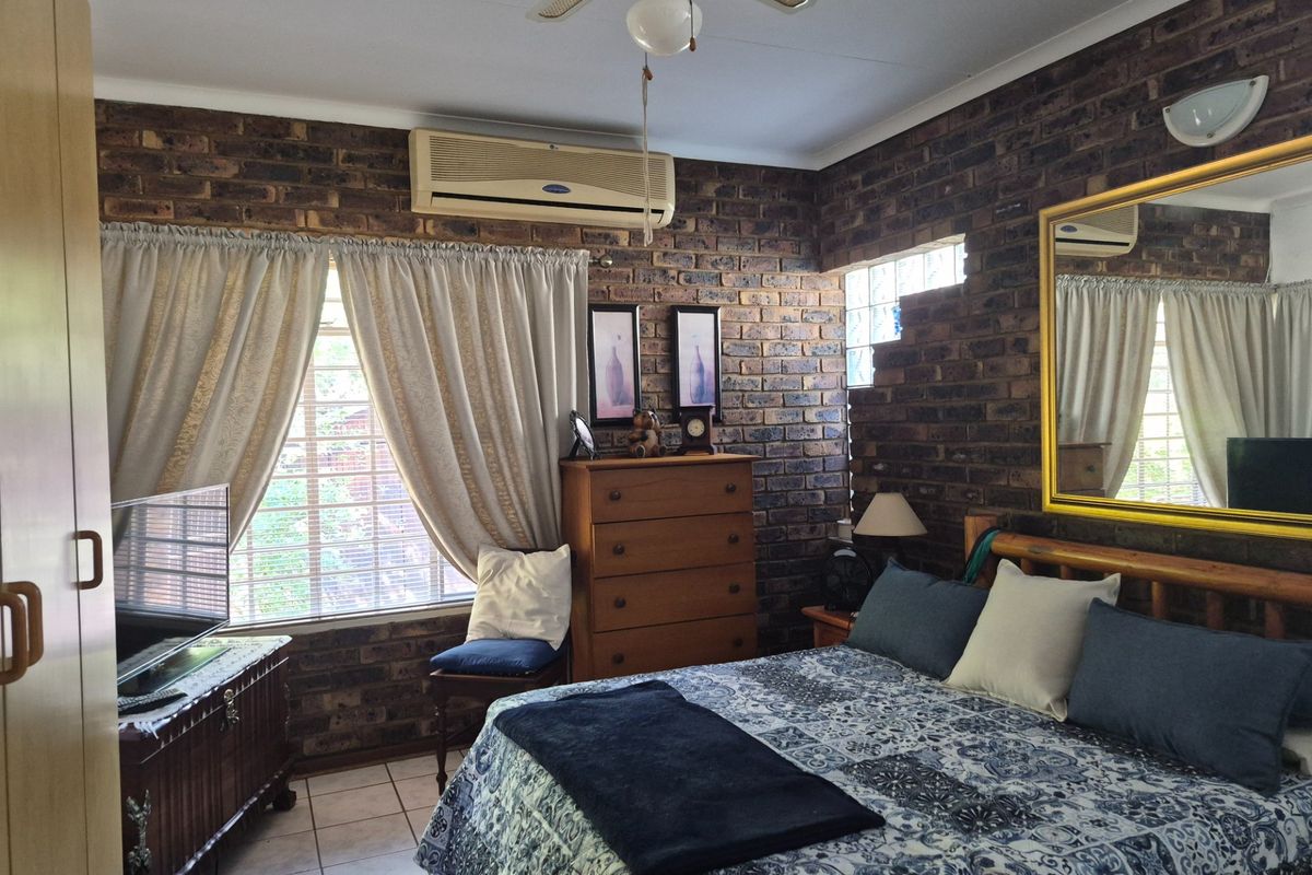 A bedroom featuring exposed brick walls, tiled flooring, a ceiling fan, and a wall-mounted air conditioning unit.