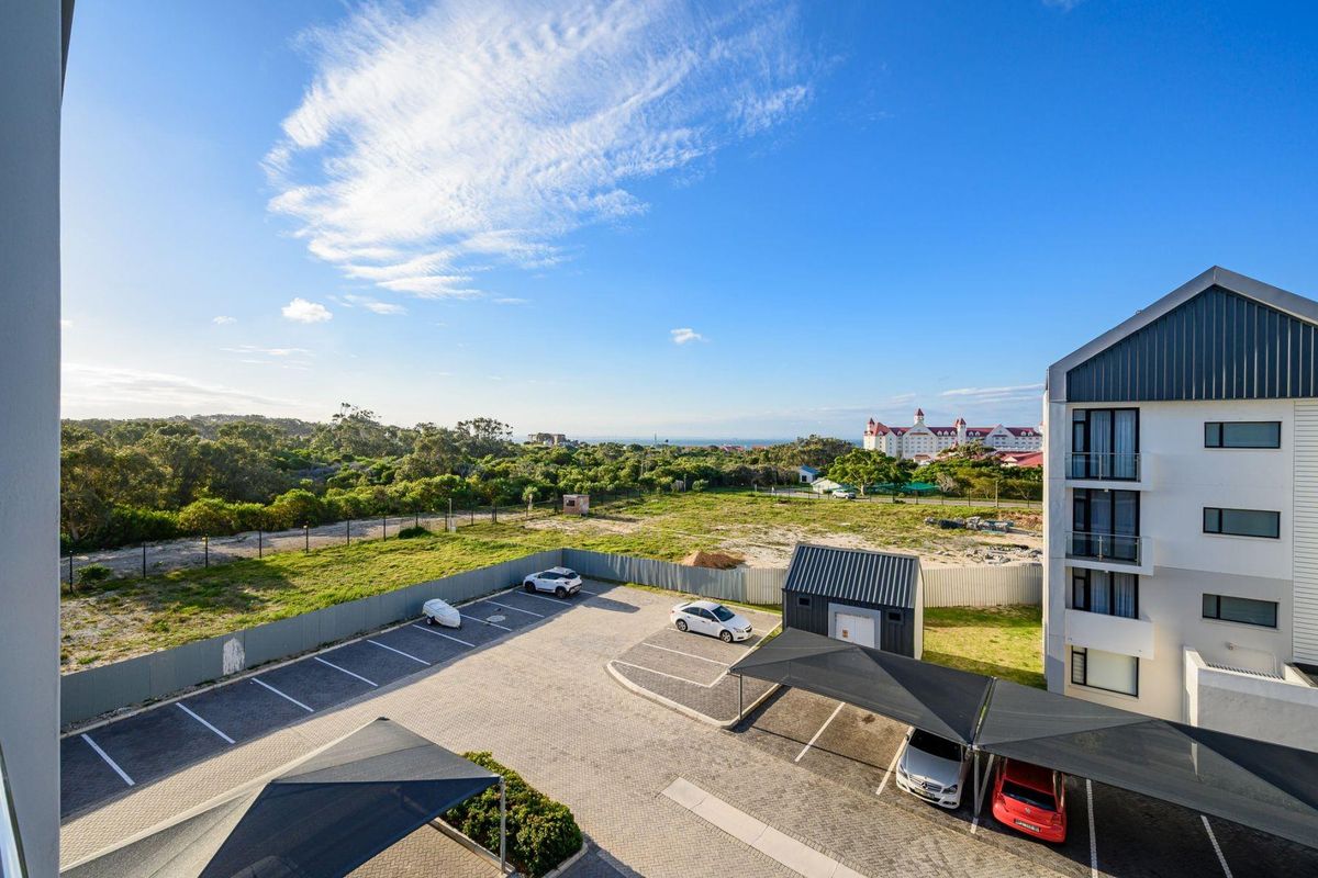 Aerial view of the apartment complex parking area featuring paved bays, shade cloth carports, and a small storage shed with surrounding landscape.