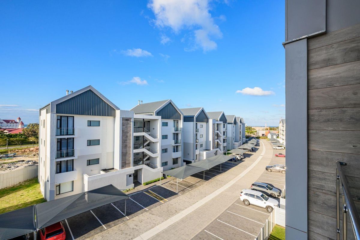 Exterior view of the apartment complex featuring modern architecture, paved parking bays with shade cloth carports, and accessible stairwells.