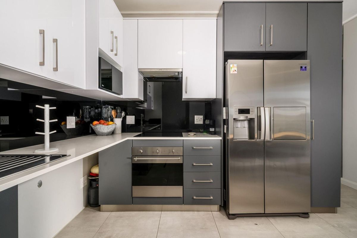 Modern kitchen featuring high-gloss white and grey cabinetry, stone countertops, integrated appliances, and a sleek black glass splashback.