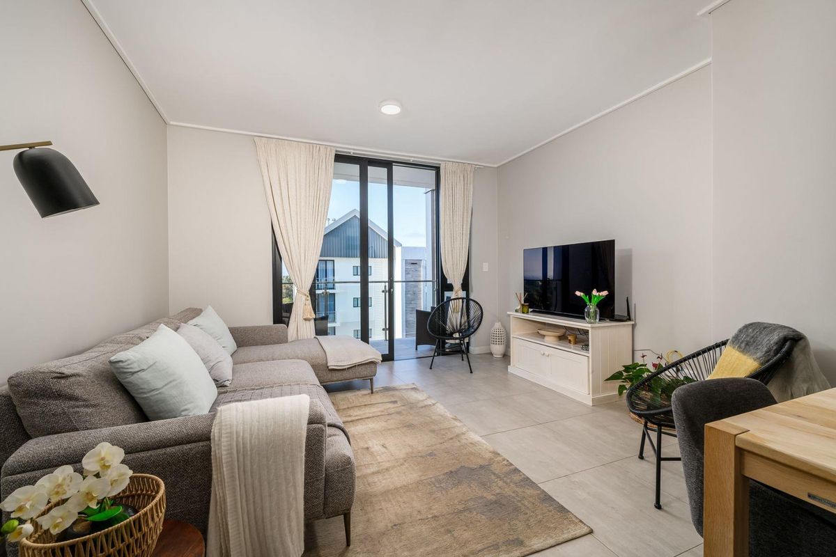 A bright and modern living room featuring large format floor tiles and a sliding glass door providing access to the balcony.