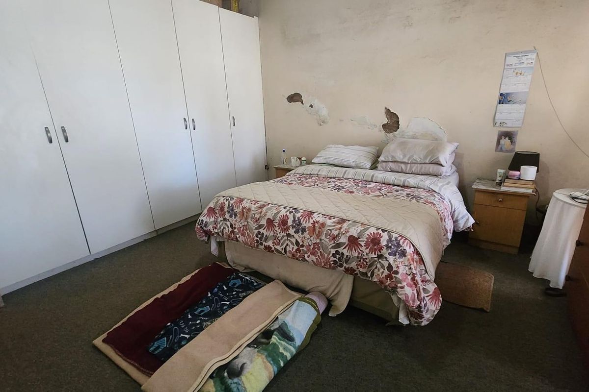A bedroom featuring built-in wardrobes and carpeted flooring, currently requiring maintenance and cosmetic repairs to the wall surfaces.