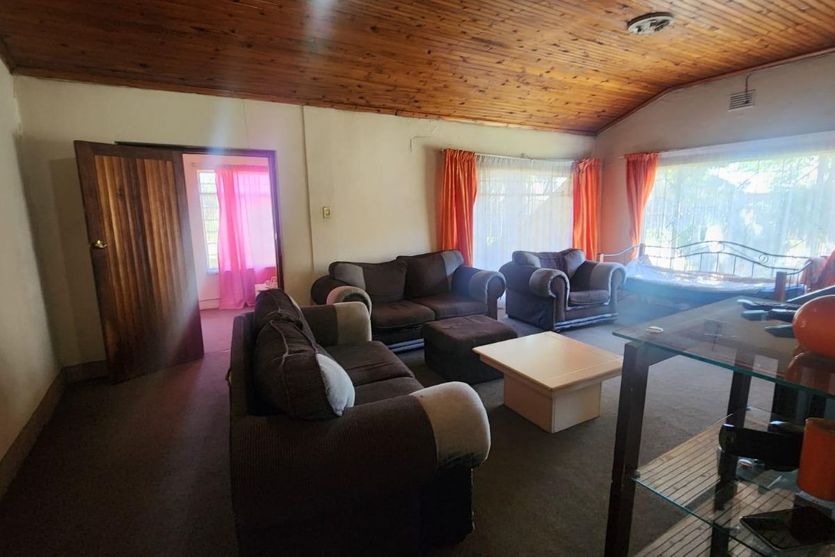 Spacious living room featuring a vaulted timber ceiling, carpeted flooring, and large windows allowing for natural light.