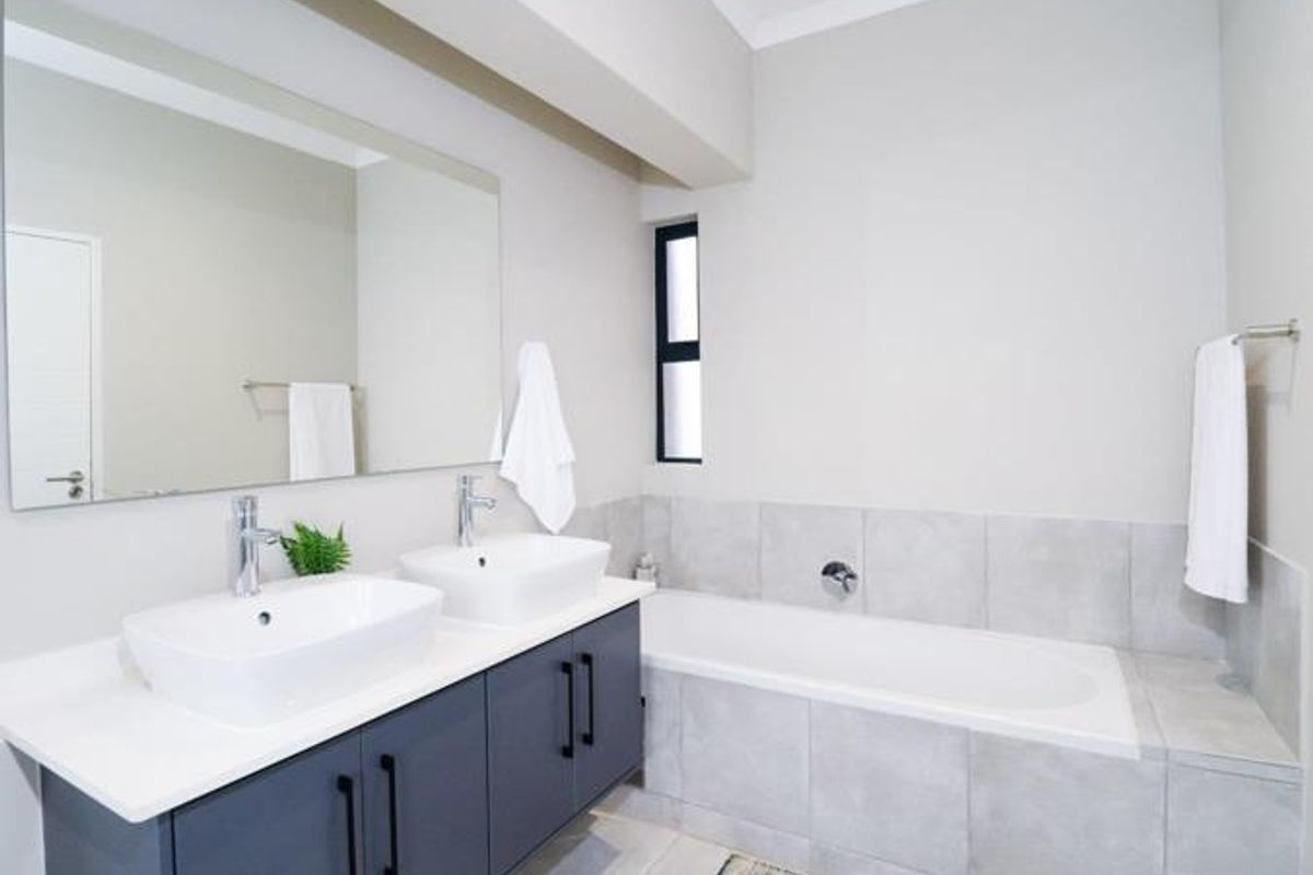 Modern bathroom featuring a double vanity with vessel sinks, a large wall-mounted mirror, and a tiled bathtub surround.