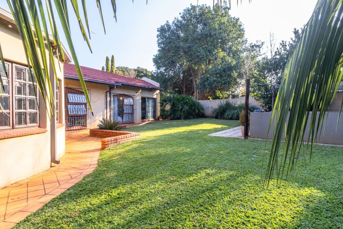 A spacious rear garden featuring a well-maintained lawn, paved walkway, and established perimeter walling, providing a private outdoor area.
