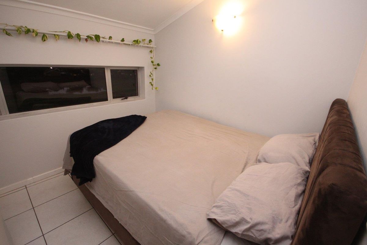 A compact bedroom featuring tiled flooring, a horizontal window, and a wall-mounted light fixture.