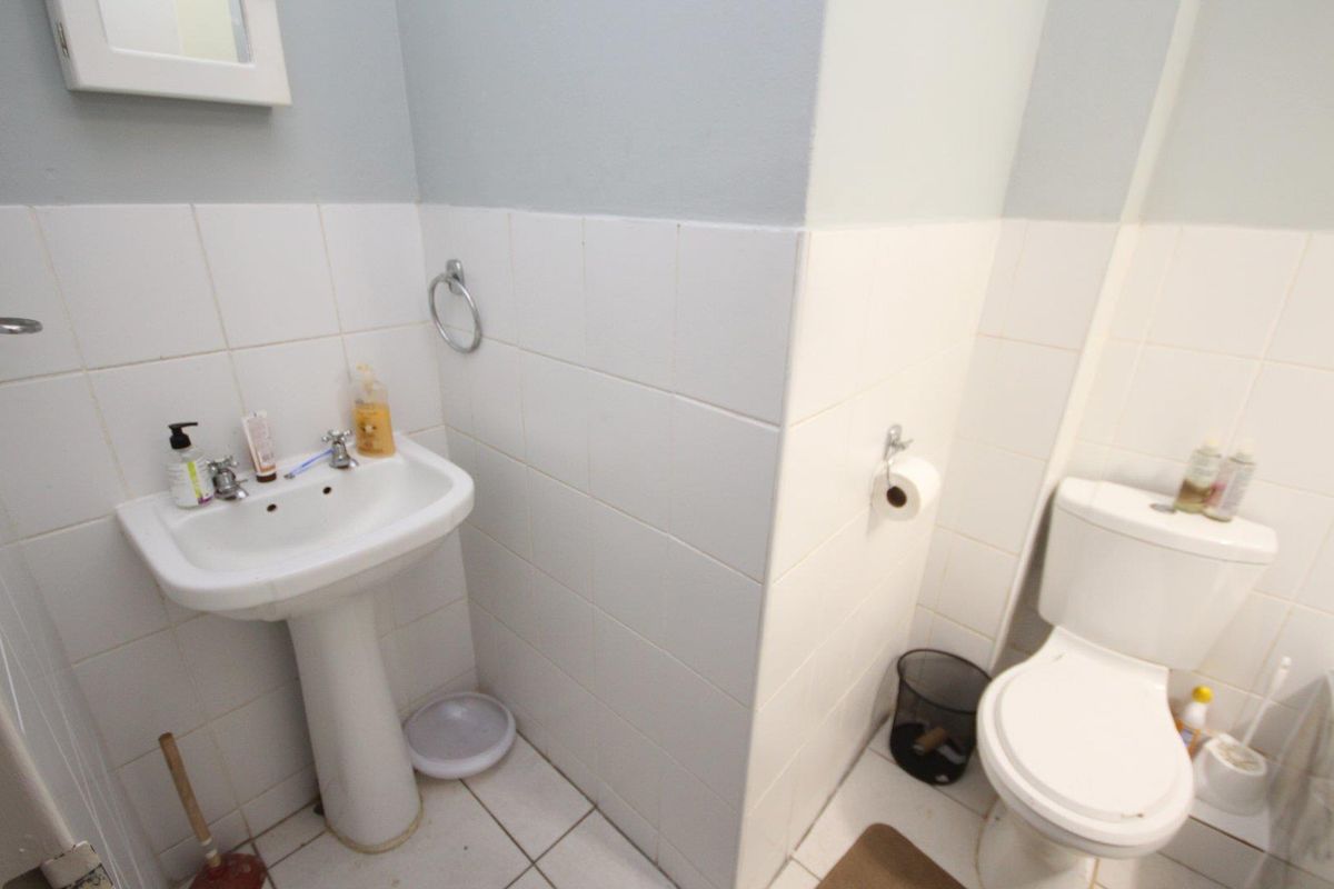 A functional bathroom featuring a pedestal basin, toilet, and white wall tiling.