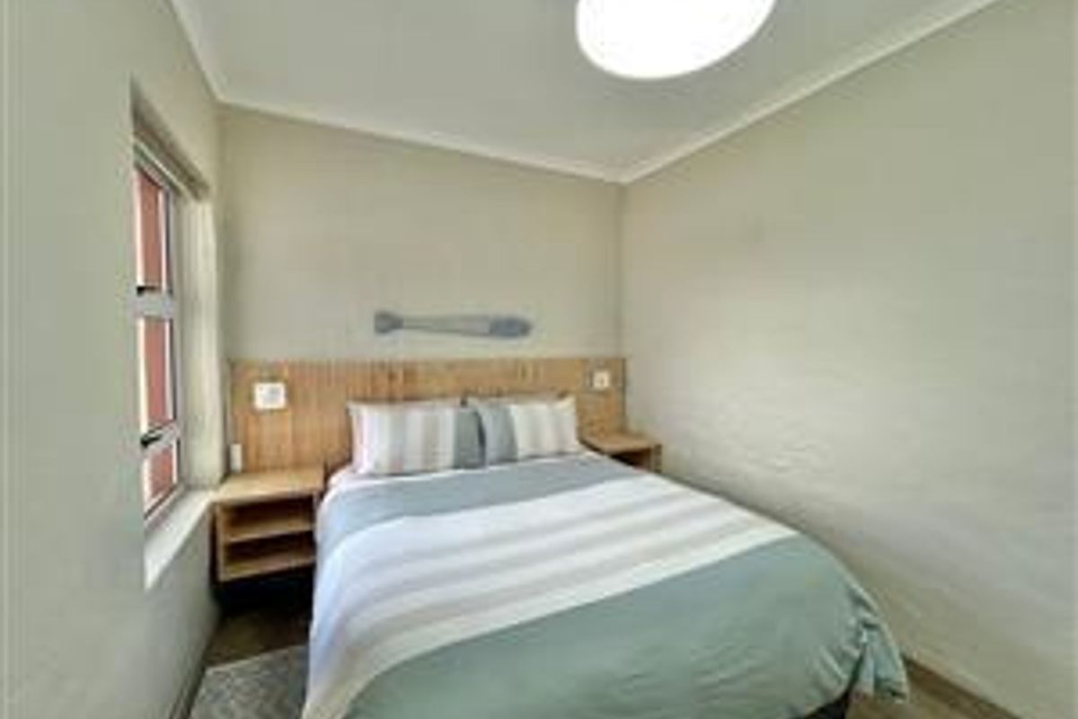 A compact bedroom featuring a built-in wooden headboard with integrated bedside shelving and a window providing natural light.