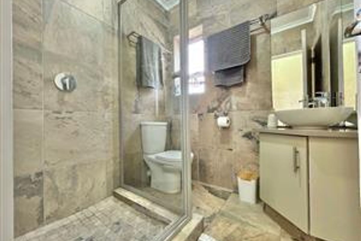 Modern bathroom featuring a glass-enclosed shower, a contemporary vanity with a vessel sink, and neutral floor-to-ceiling wall tiling.