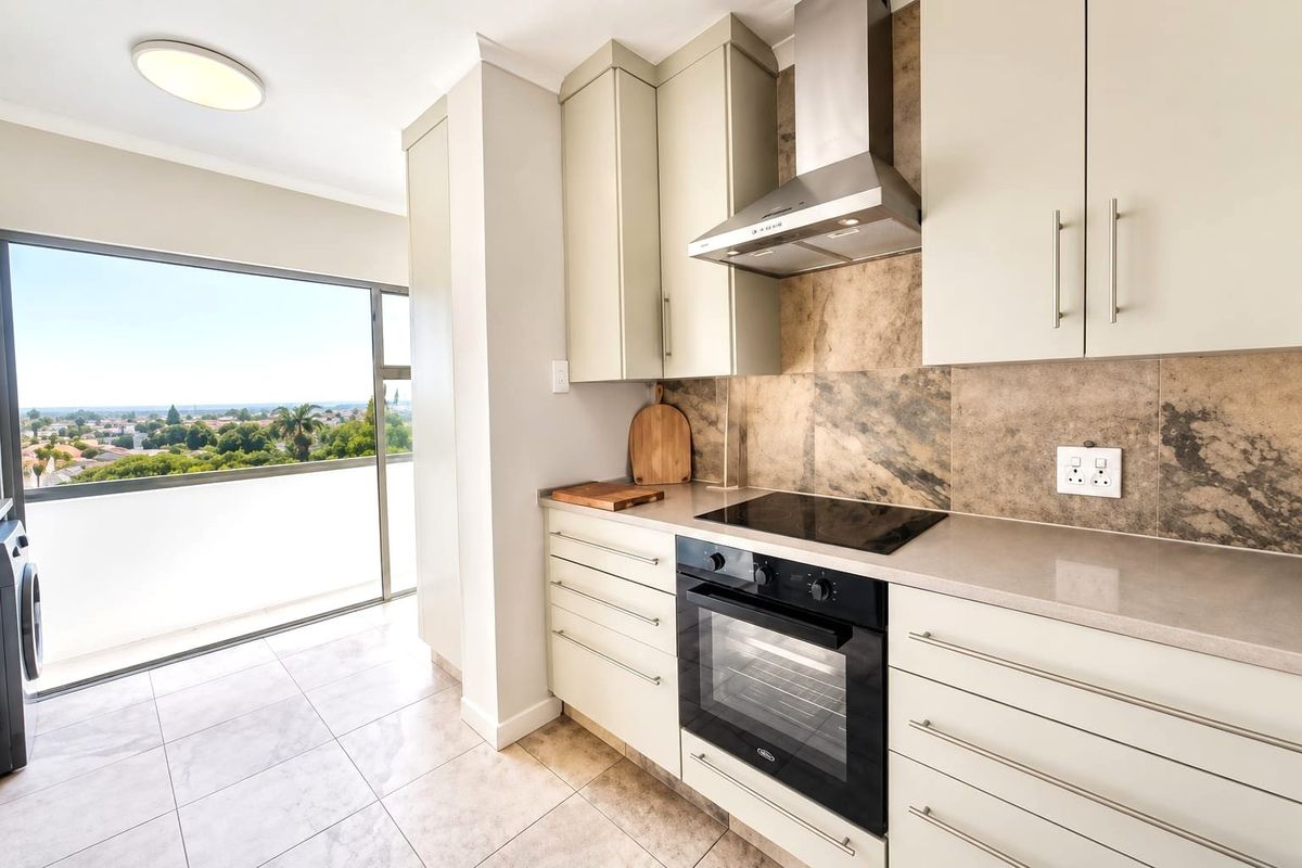 Modern kitchen featuring sleek cabinetry, stone countertops, integrated appliances, and a tiled backsplash, with direct access to a balcony offering scenic views.