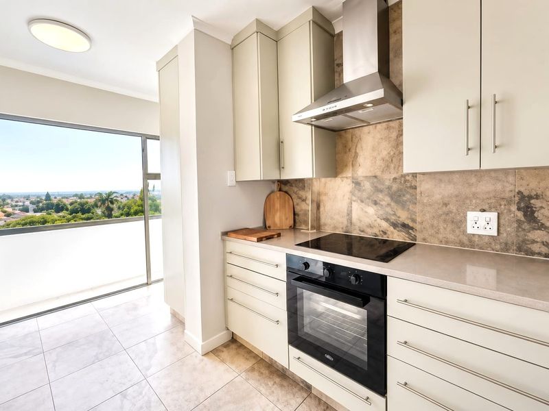 Modern kitchen featuring sleek cabinetry, stone countertops, integrated appliances, and a tiled backsplash, with direct access to a balcony offering scenic views.